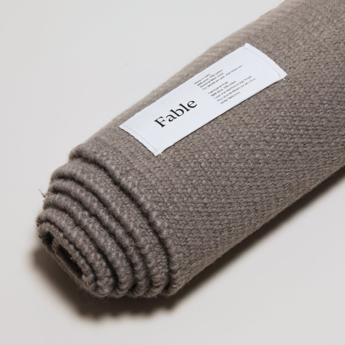 A rolled-up gray knit blanket with a white label showing the brand name "Fable.