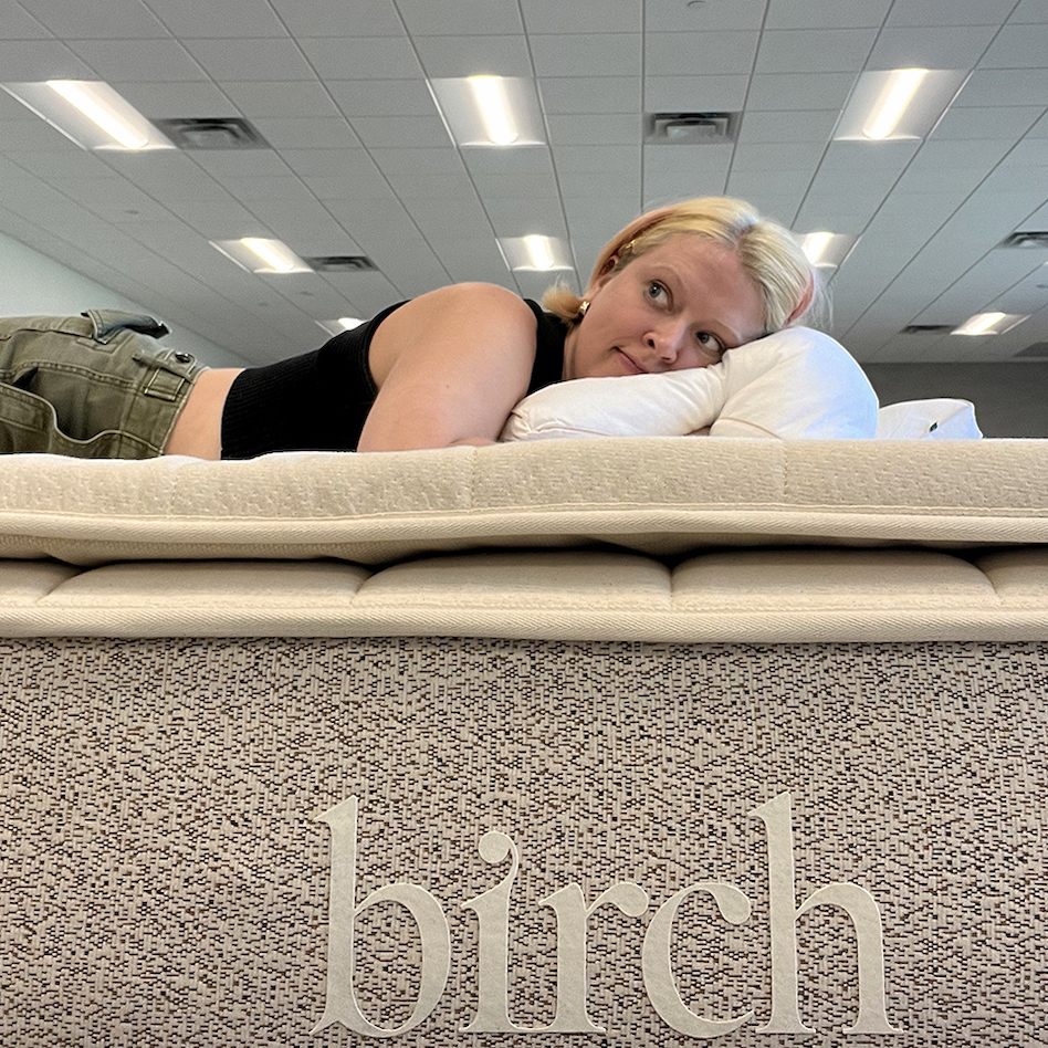 Emily McGowan relaxes on a mattress with their head on a pillow. The word "birch" graces the side of this nontoxic, organic mattress.
