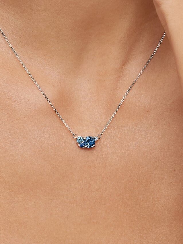A close-up of a woman's neck wearing a delicate silver chain necklace with a small blue gemstone pendant.