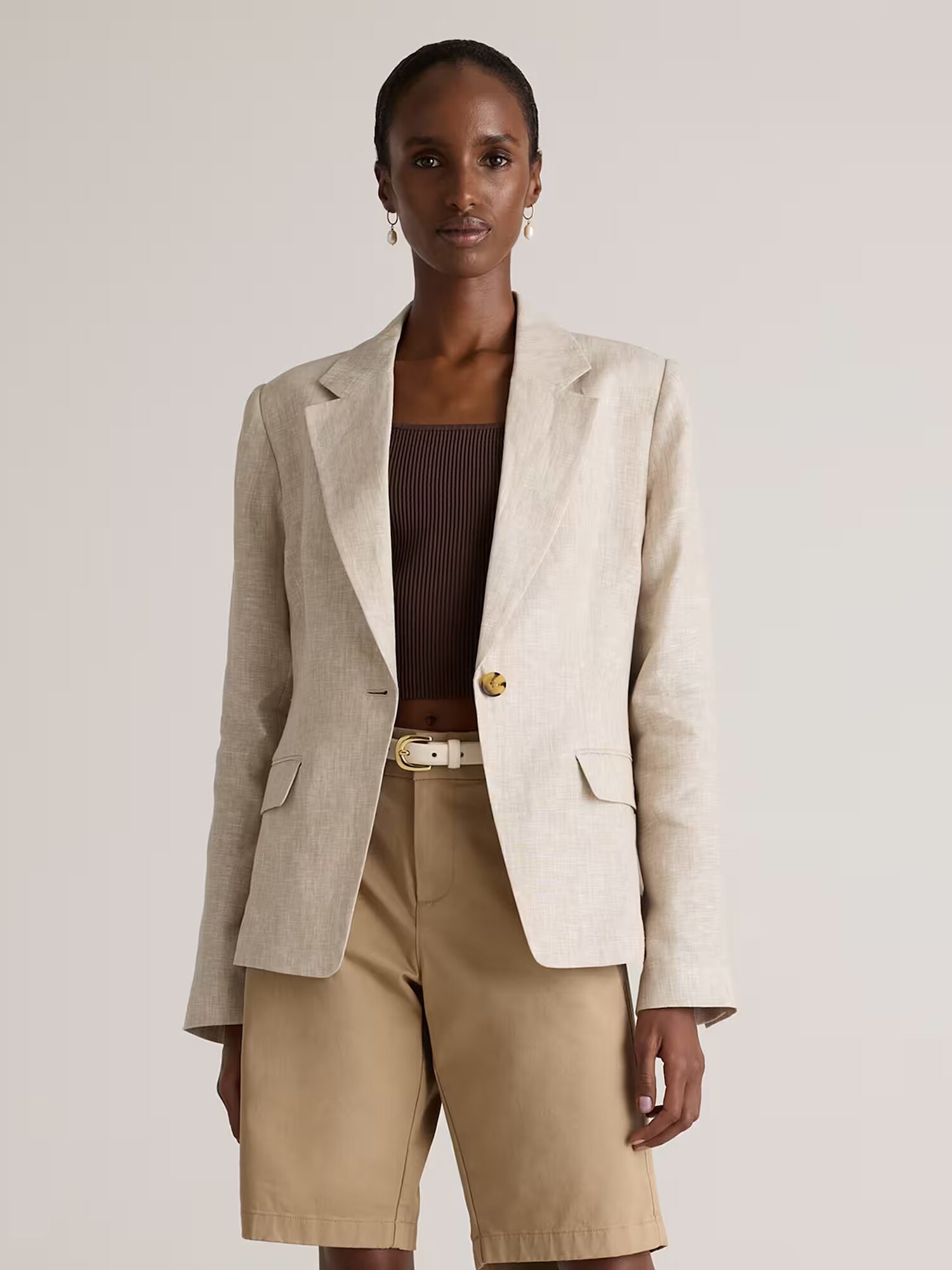 Person wearing a beige blazer over a brown ribbed crop top and tan knee-length shorts, standing against a plain light background.