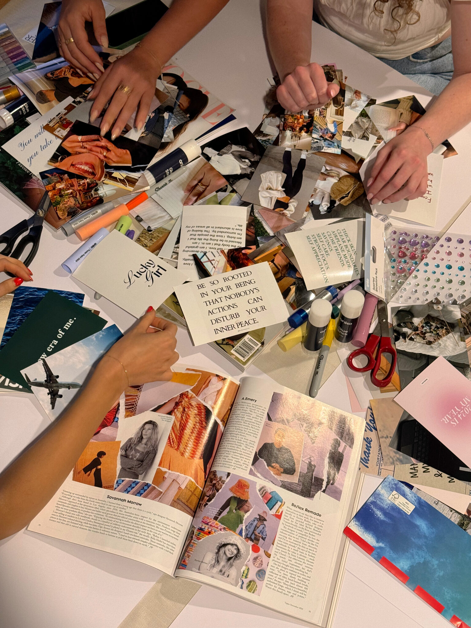 Four people work together on a table covered with magazines, cut-out images, scissors, glue, and collage materials.