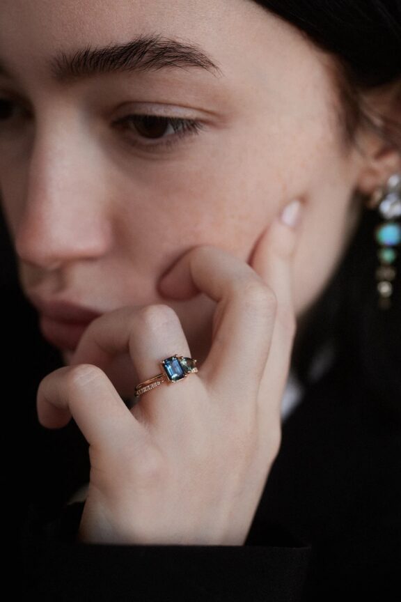 Close-up of a person touching their cheek while wearing a gold ring with a rectangular gemstone on their finger.