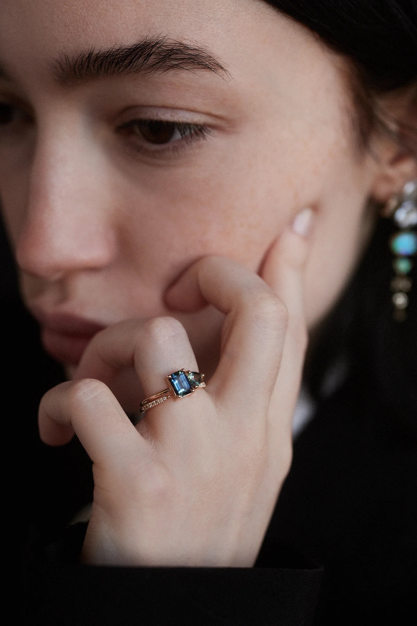 Close-up of a person touching their cheek while wearing a gold ring with a rectangular gemstone on their finger.