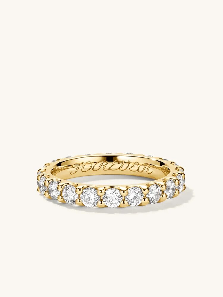 A gold eternity ring with multiple small round diamonds set around it. The inner band is engraved with the word "FOREVER.