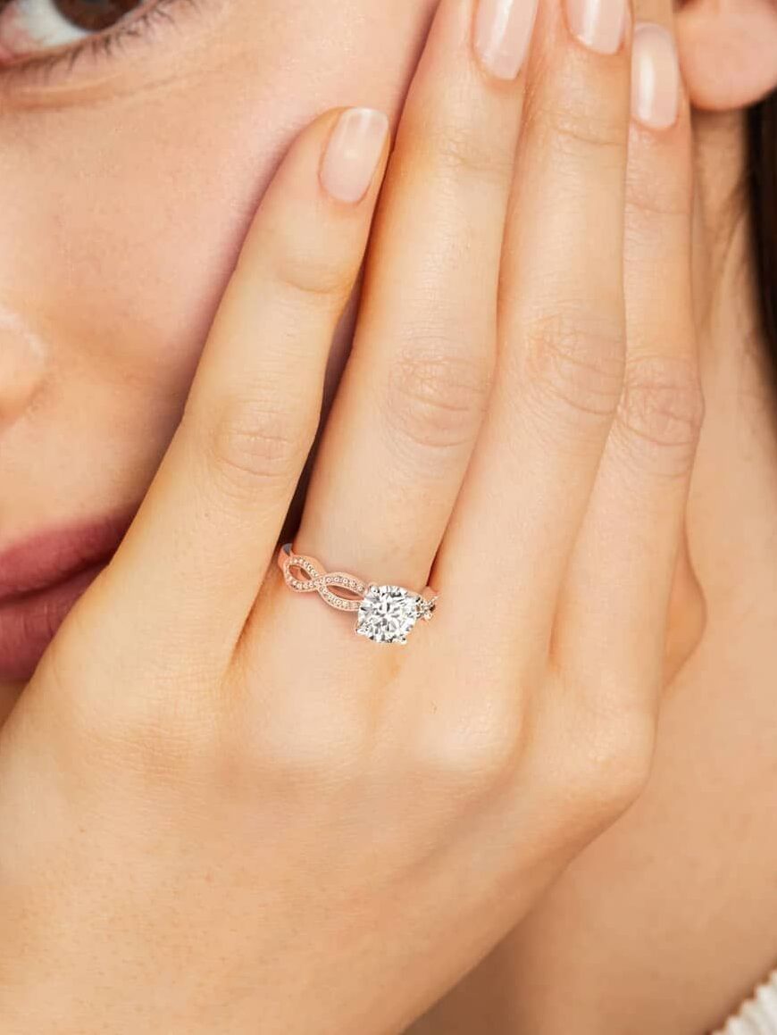 A person with long brown hair displays a diamond ring on their hand, lightly touching their face.