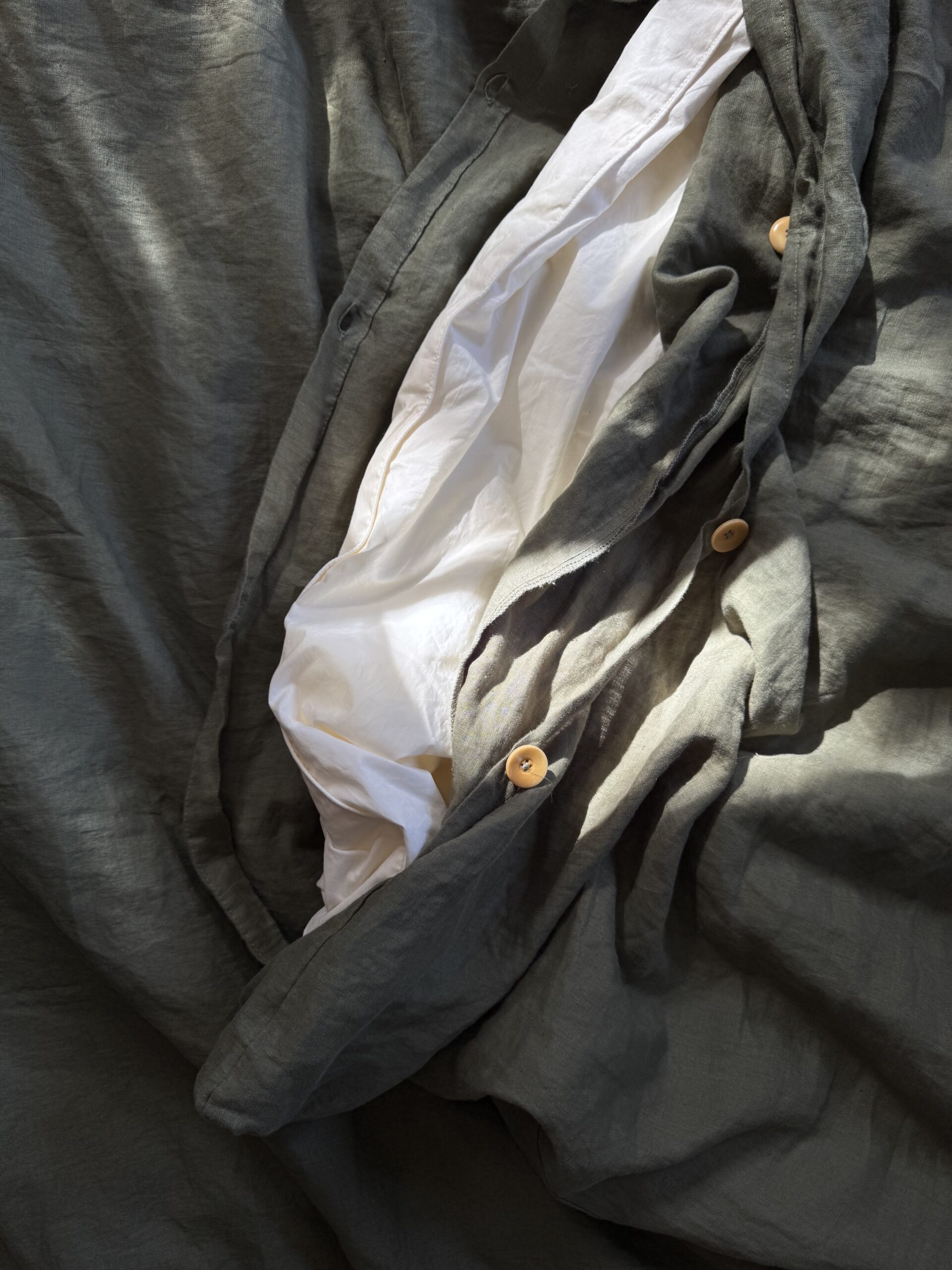 A close-up of a crumpled, open gray fabric with wooden buttons, revealing a white inner fabric layer beneath.