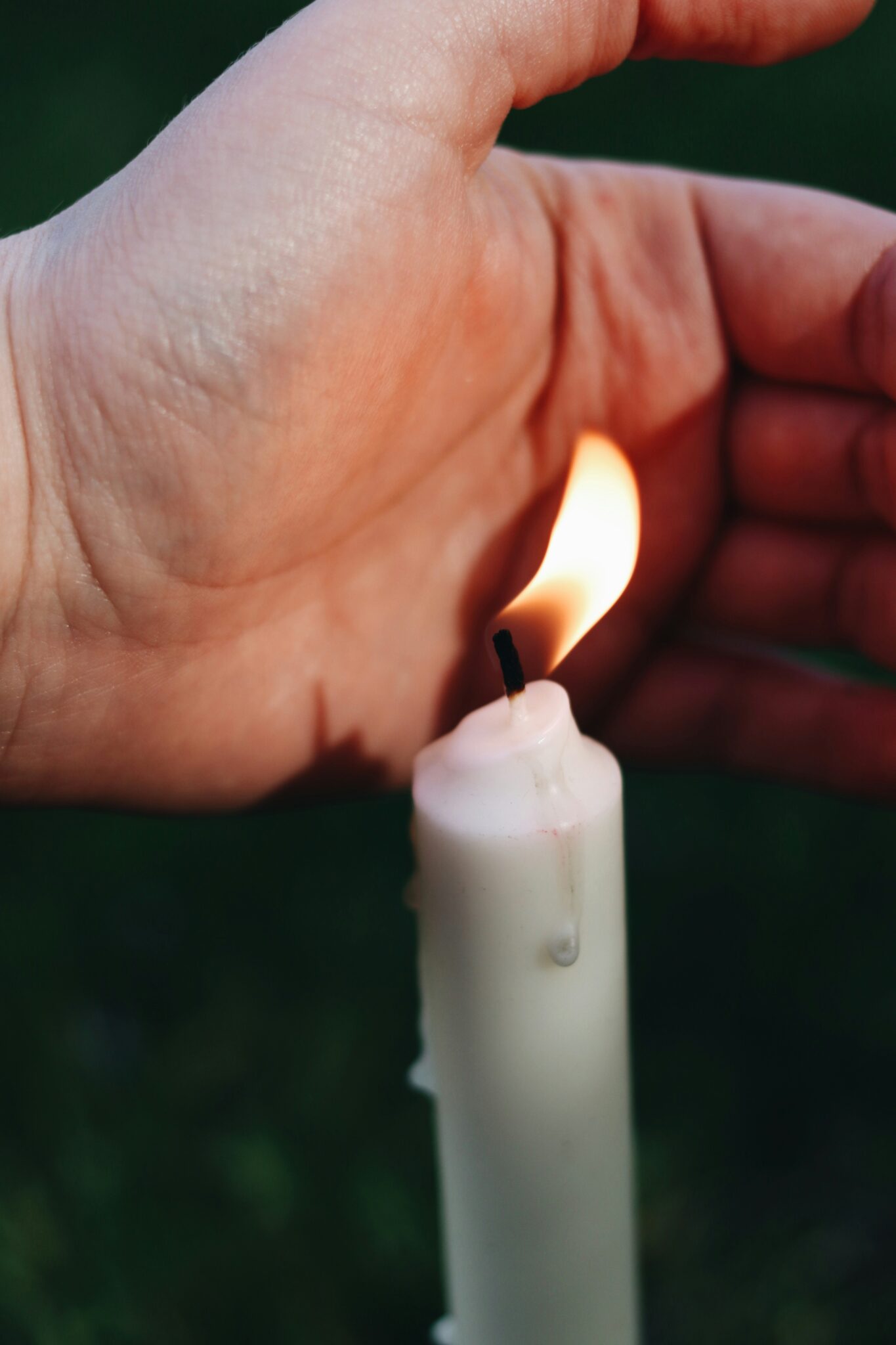 A hand is held near the flame of a lit white candle, partially shielding the flame.
