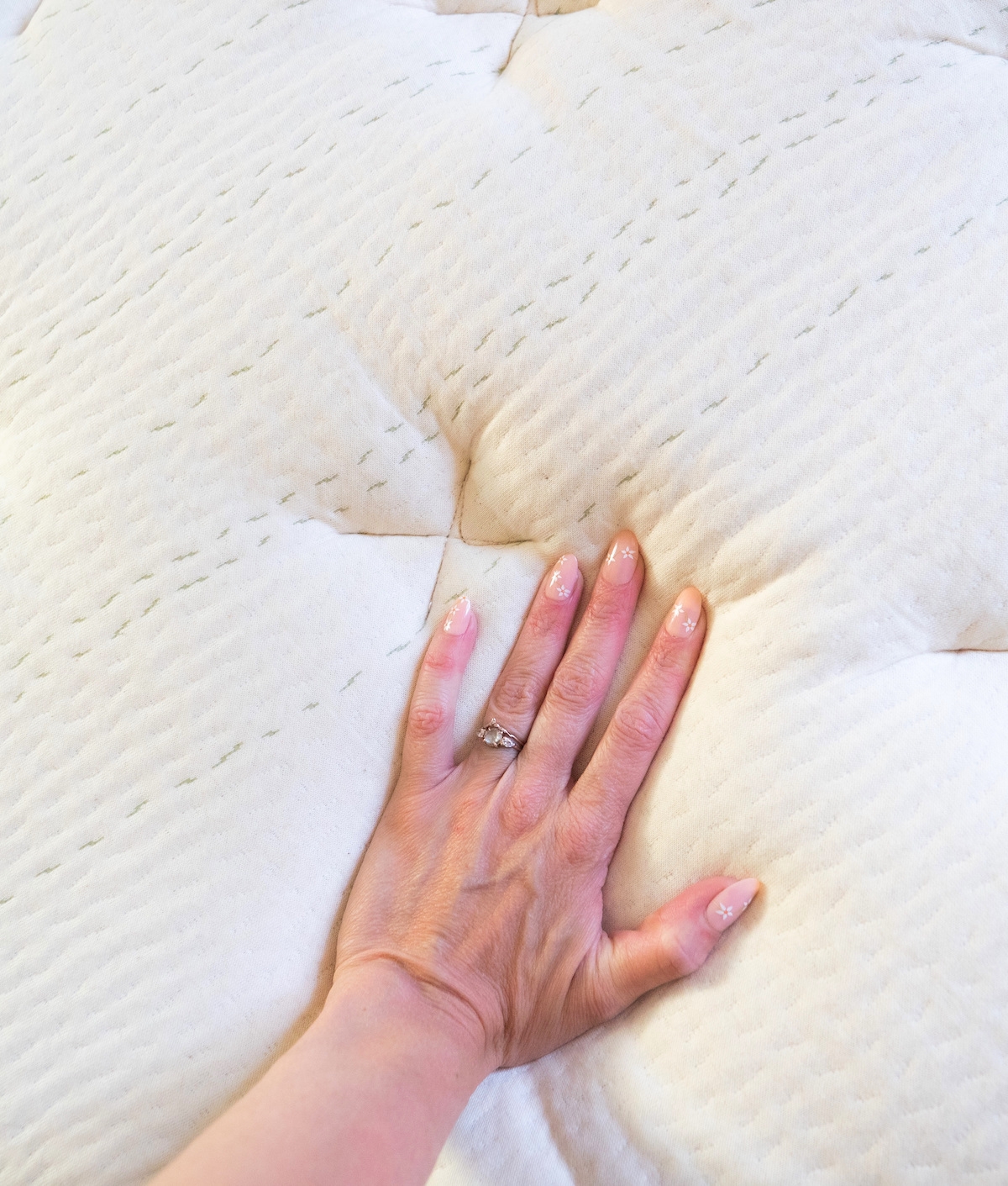 Reviewer Courtney Jay Higgins's hand presses down on a beige, nontoxic Leesa mattress, revealing its texture and softness.