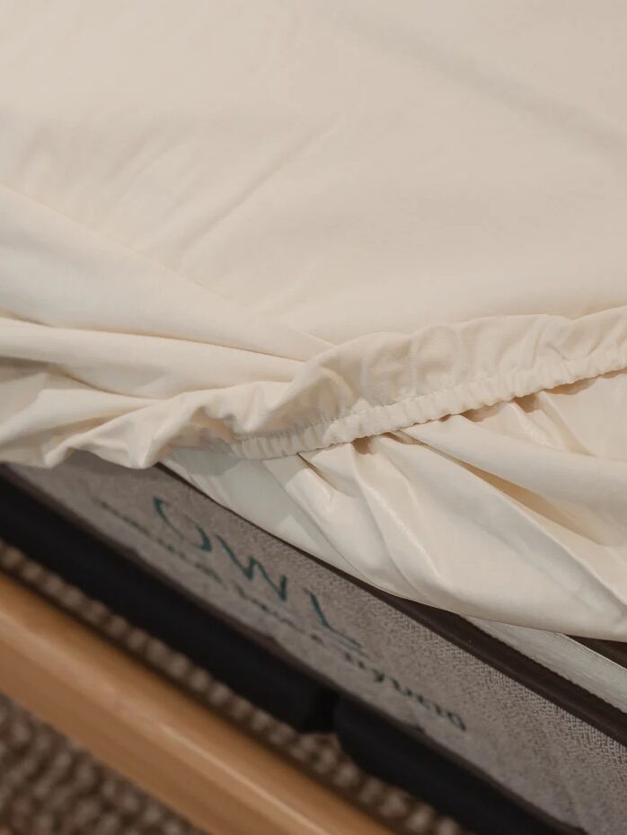 Close-up of a beige fitted sheet partially pulled over a mattress corner with visible elastic.