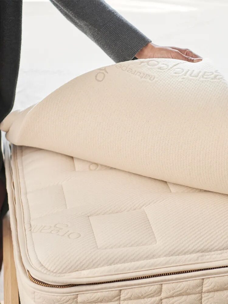 Person lifting the corner of a beige mattress pad on top of a mattress.