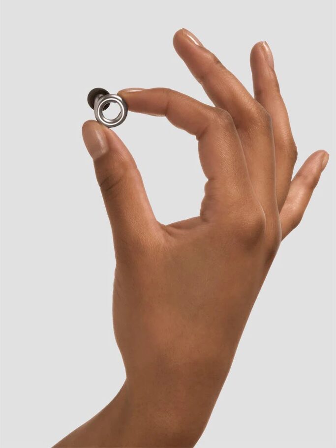 A hand holding a small, round metallic object between the thumb and index finger against a plain light background.