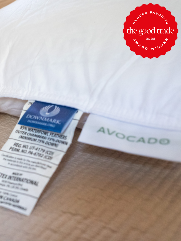 Close-up of pillow corner showing product tags labeled "DOWNMARK" and "AVOCADO," with a red "The Good Trade 2026 Award Winner" badge in the top right corner.