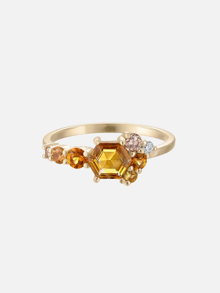 Gold ring with a central hexagonal yellow gemstone, surrounded by smaller round gemstones in shades of amber, peach, and white.
