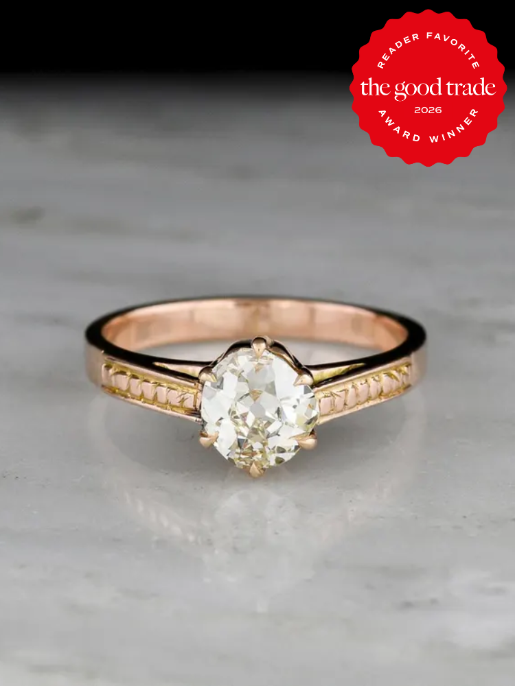 A gold engagement ring with a large oval diamond is displayed on a marble surface. A red badge in the corner reads, "The Good Trade Reader Favorite Award Winner 2026.