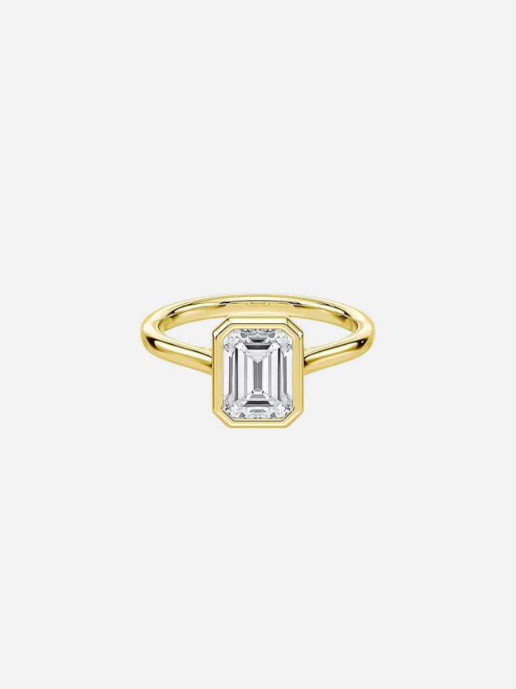 Gold ring with an emerald-cut diamond in a bezel setting on a plain band.