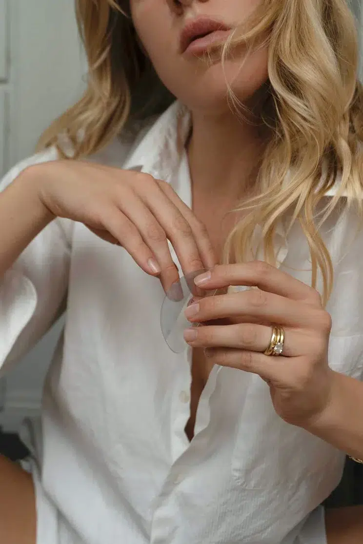 A person in a white shirt with blonde hair holds a translucent object with both hands; they are wearing gold rings on one hand.